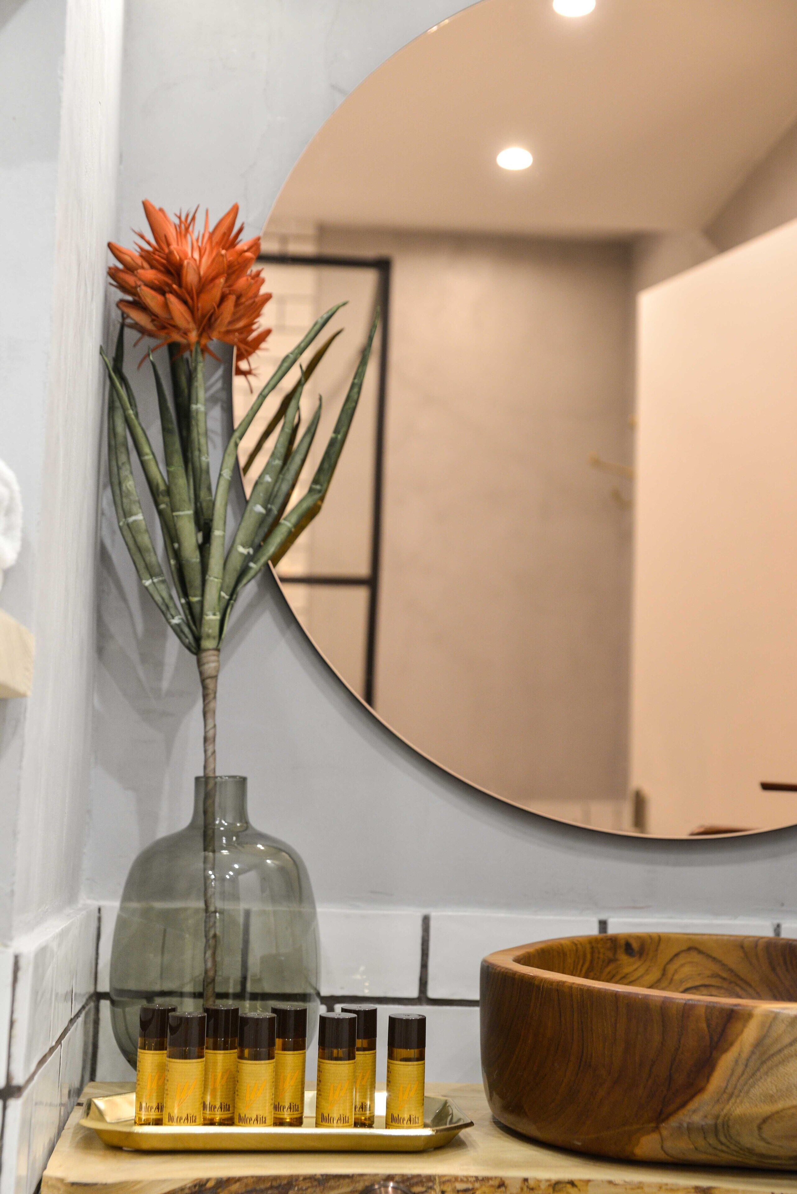 Un baño con un espejo grande, un cuenco de madera y un florero con una planta.