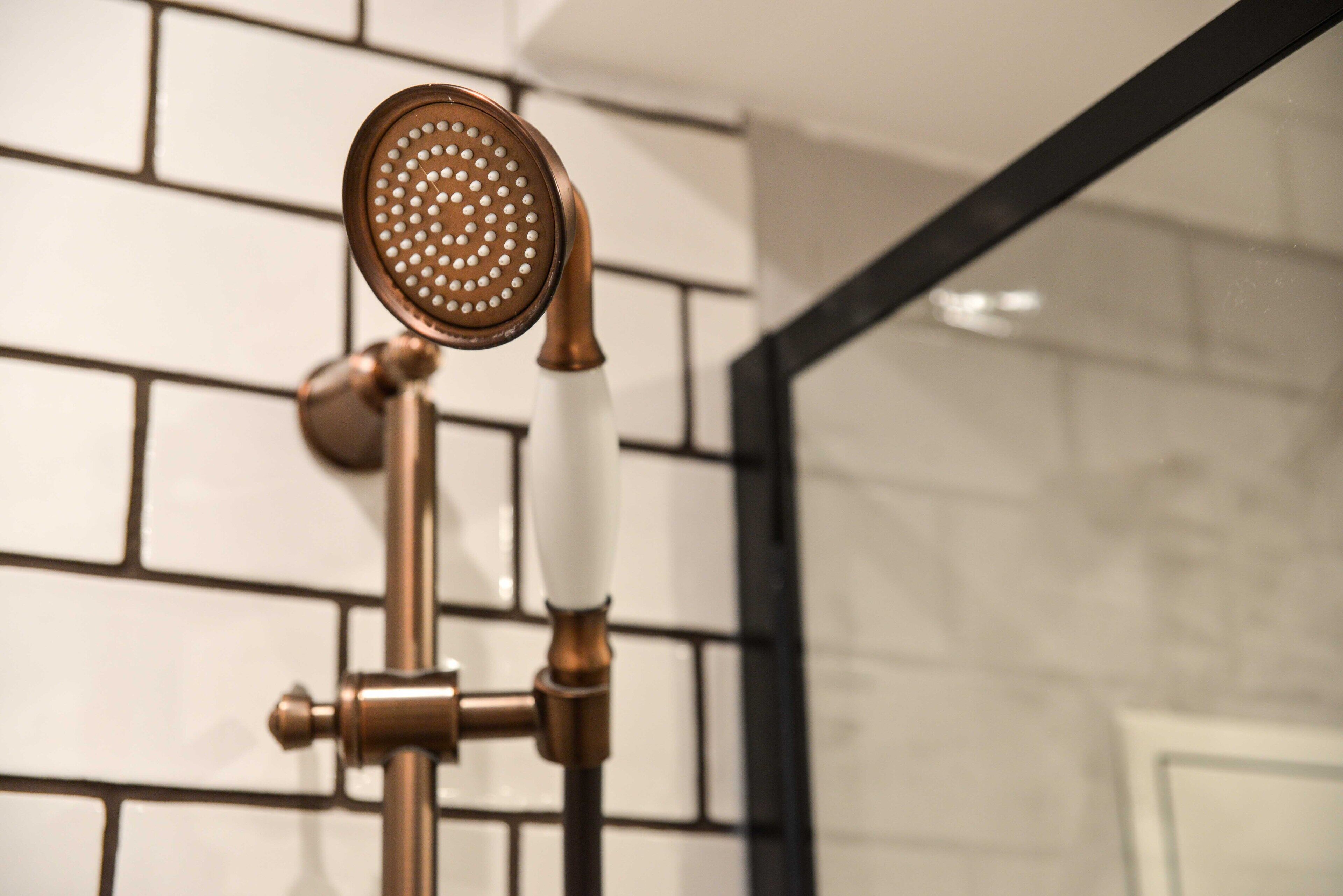 A showerhead with a perforated head, mounted on a wall with a tiled backsplash.