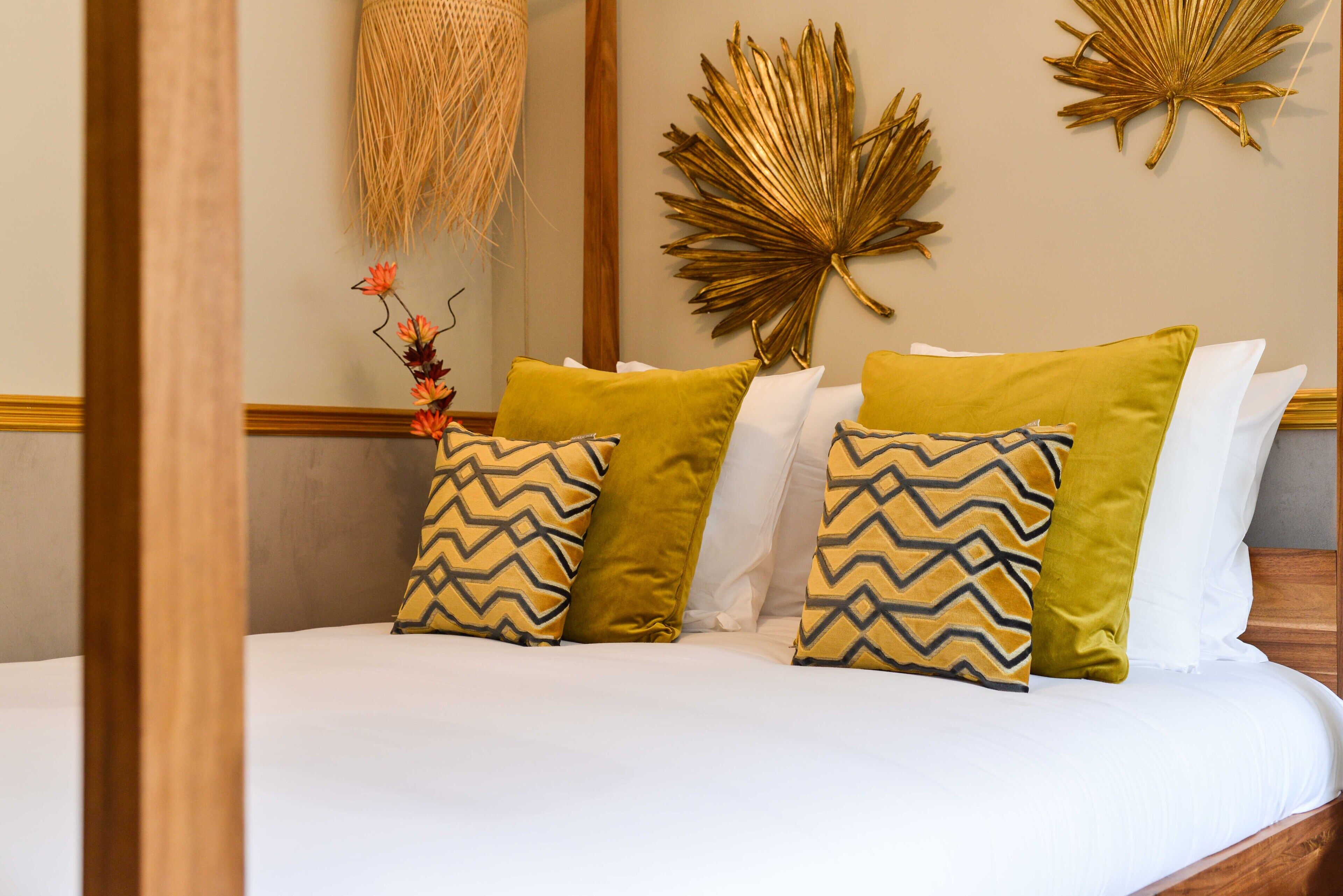 A neatly made bed with patterned pillows, a decorative wall hanging, and a large golden leaf decoration.