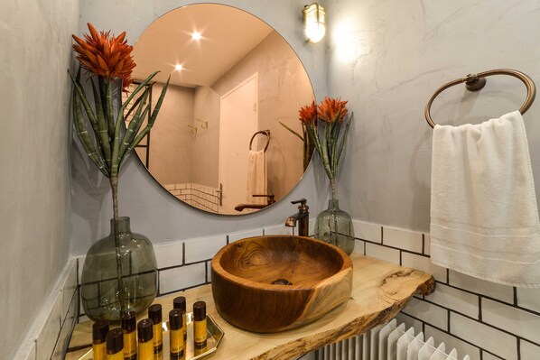 Un baño con un lavamanos de madera redondo, dos espejos grandes y un perchero para toallas.