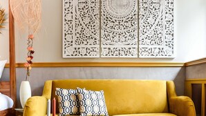 A room with a yellow sofa, a round wooden table with breakfast items, and a decorative wall panel. - The Majestic Garden Suite (Paris)