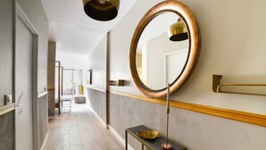 A hallway with a marble floor, a round mirror with a gold frame, and a small table with a gold bowl. - The Majestic Garden Suite (Paris)