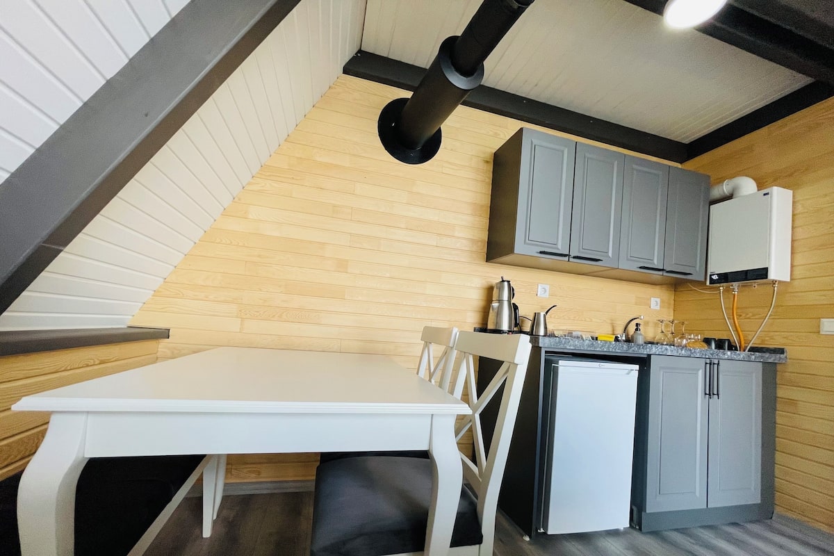 A compact kitchen with a white table and chairs, grey cabinets, and a small refrigerator.
