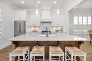 A spacious kitchen with a large island, white cabinetry, stainless steel appliances, and pendant lighting.