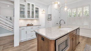 Une cuisine moderne avec des meubles blancs, un grand îlot central doté d’un évier et un escalier menant à un autre niveau.