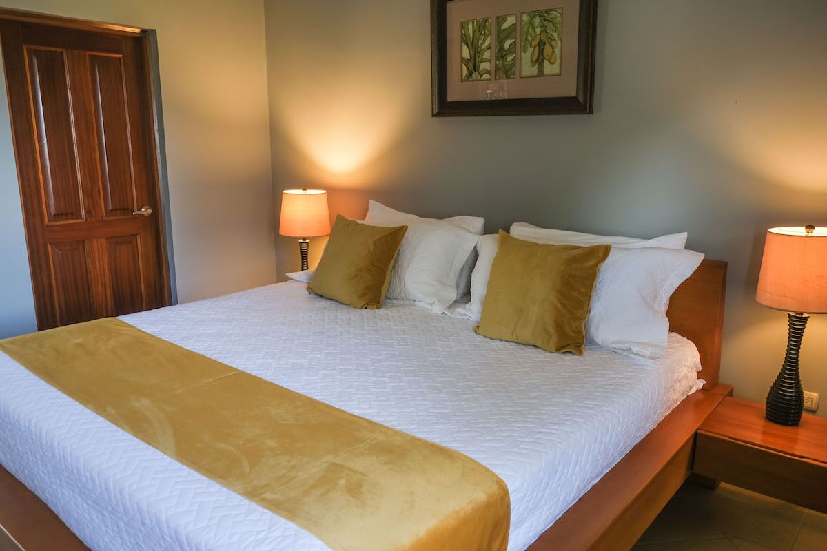 A neatly made bed with a white and yellow bedspread, two bedside lamps, and a framed artwork on the wall.