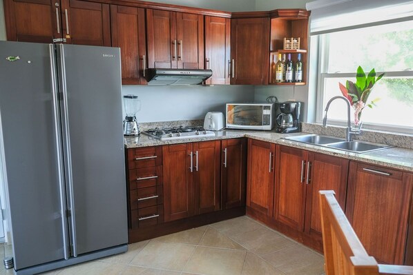 A modern kitchen with wooden cabinets, a stainless steel refrigerator, a microwave, and a coffee maker.