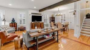 A spacious living room with a wooden dining table, a sofa, and a television.