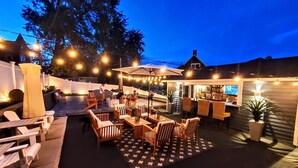 An outdoor patio area with wooden furniture, string lights, and a bar area.