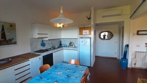 A compact kitchen with white cabinets, a stove, and a dining area with a table. - Castiglioncello Baia del Quercetano, the sea in the eyes. (Rosignano Solvay-Castiglioncello)