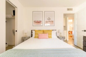 Une chambre d’hôtel avec un grand lit, deux tables de chevet avec des lampes, une armoire et deux tableaux encadrés au mur.