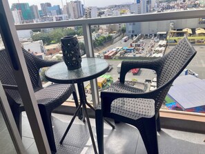 A balcony with two wicker chairs and a small round table, overlooking a busy street with buildings and vehicles. - Gorgeous 2 Bedroom Flat in Nice Commercial Area (San Miguel)