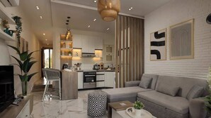 Een moderne woonkamer met een grijze bank, een salontafel en een televisie. Achtergrond toont een keuken met witte kasten en een hangende lamp.