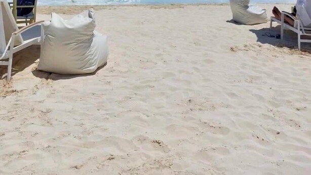 Een strand met witte ligbedden en gestreepte parasols, een helderblauwe lucht en een kalme zee.