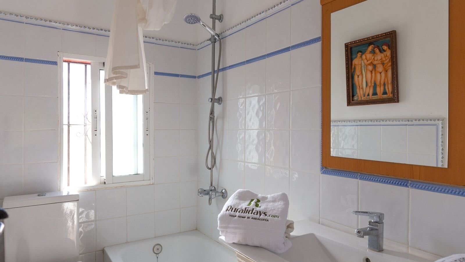 A bathroom with a bathtub, a shower, and a window. There is a towel with a logo on it.