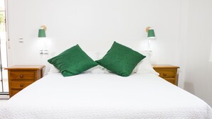 A neatly made bed with a white quilt and two green pillows, flanked by wooden nightstands with green lamps. - Family house in a quiet university neighborhood (Málaga)