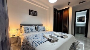 Ein ordentlich bezogenes Bett mit einer Decke, einer Nachttischlampe und einem Spiegel.