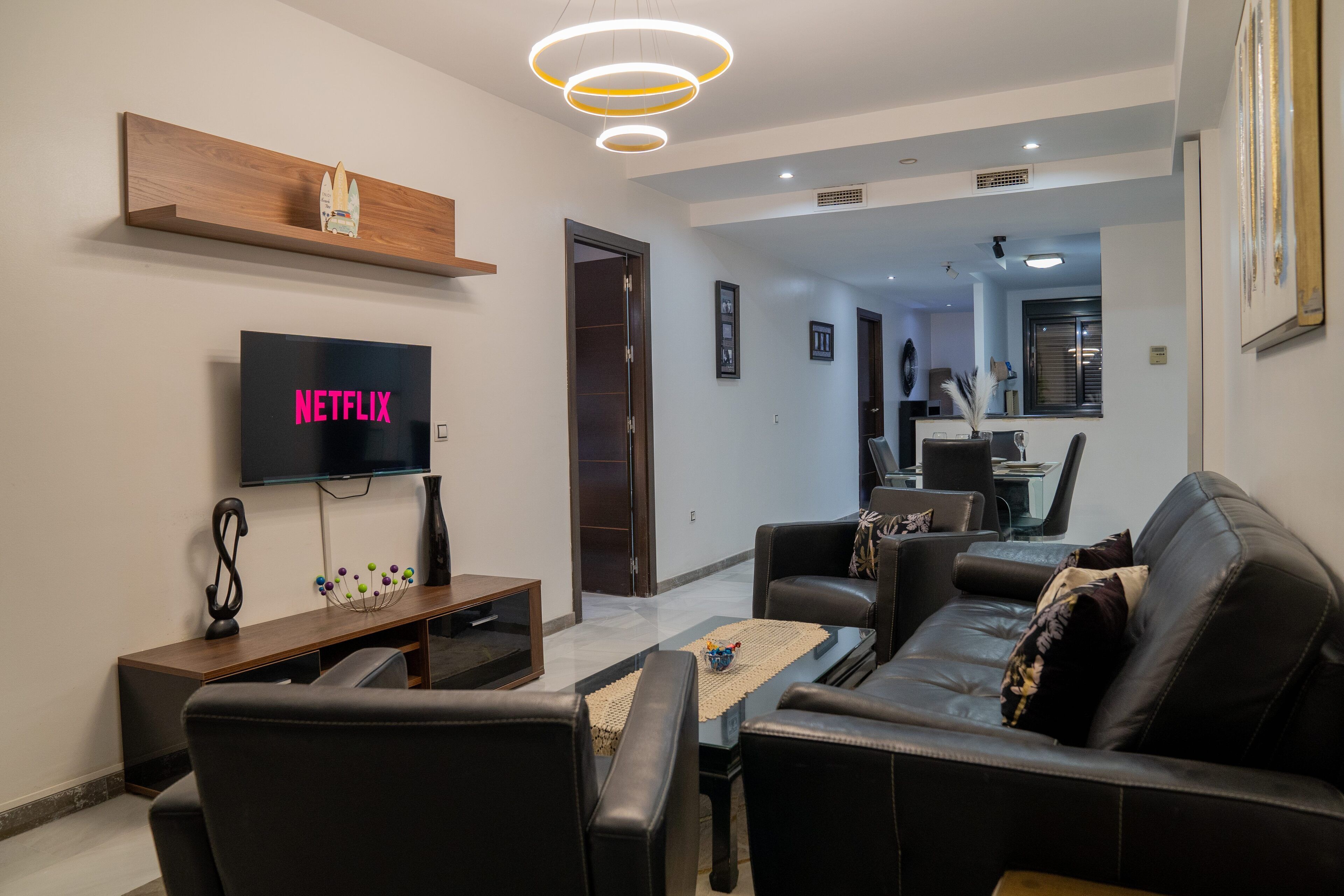 Una sala de estar moderna con un televisor de pantalla plana, una estantería de madera, un sofá de cuero negro y una mesa de centro.