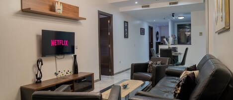 Una sala de estar moderna con un televisor de pantalla plana, una estantería de madera, un sofá de cuero negro y una mesa de centro.