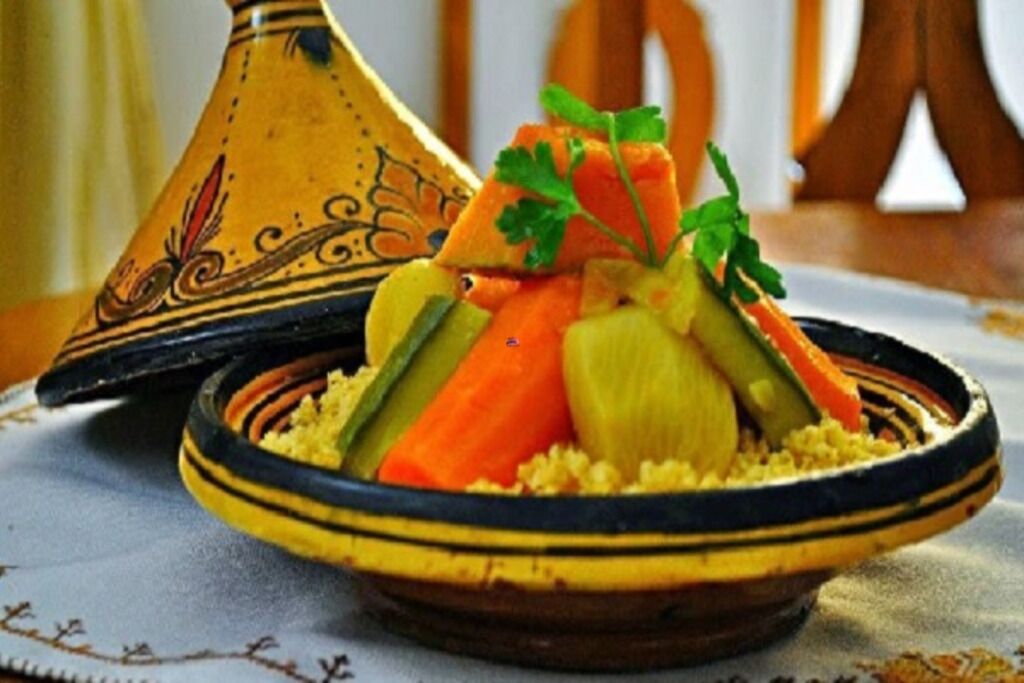 Ein traditionelles marokkanisches Tajine mit Gemüse und Kuskus, serviert auf einem Tisch mit gemustertem Tischläufer.
