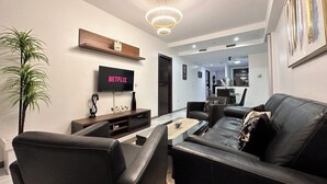 Ein modernes Wohnzimmer mit einem schwarzen Ledersofa, einem Couchtisch und einem an der Wand befestigten Flachbildfernseher.