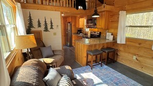 Interior acogedor de una cabaña con techo de madera, comedor, cocina y sala de estar con sofá y cojines.