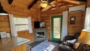 Interior de una cabaña de madera con chimenea, sofá, televisión y zona de comedor.