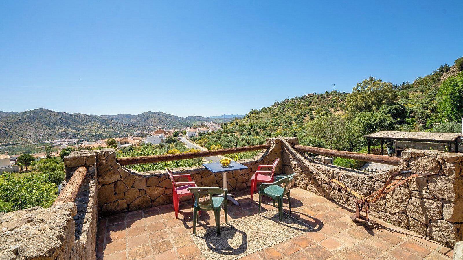Une terrasse en pierre avec une table et des chaises, d’où l’on a vue sur un village et des montagnes.