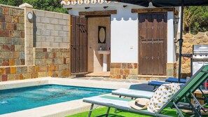 Una piscina con sillas de descanso, una parrilla y un muro de piedra.