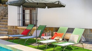 Un área junto a la piscina con sillas de descanso, una mesa con una bebida y una sombrilla.