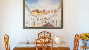 A dining area with a table, chairs, a painting, and a vase with flowers. - Casa Rural La Promesa Álora by Ruralidays (Málaga)