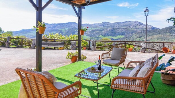 A covered outdoor seating area with wicker furniture, a table with a glass top, and potted plants.