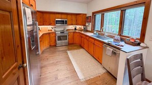 Una cocina con armarios de madera, electrodomésticos de acero inoxidable, un ventanal y vistas a árboles.