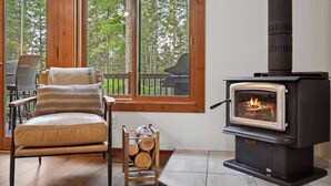 Un cuarto acogedor con chimenea, una silla y una ventana con vistas a árboles.