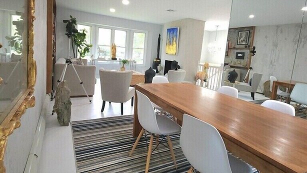 A modern dining area with a wooden table and white chairs, a striped rug, and a large mirror on the left. - Artistic get away (Hampton Bays)