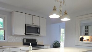 A modern kitchen with white cabinetry, a central island, a microwave, and pendant lighting. - Artistic get away (Hampton Bays)