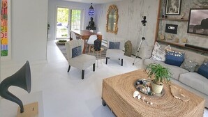 A modern living room with a sofa, coffee table, and chairs. There is a dining area with a table and chairs. - Artistic get away (Hampton Bays)