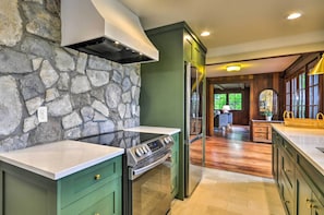 Una cocina con pared de piedra, armarios verdes, estufa de acero inoxidable y un refrigerador.