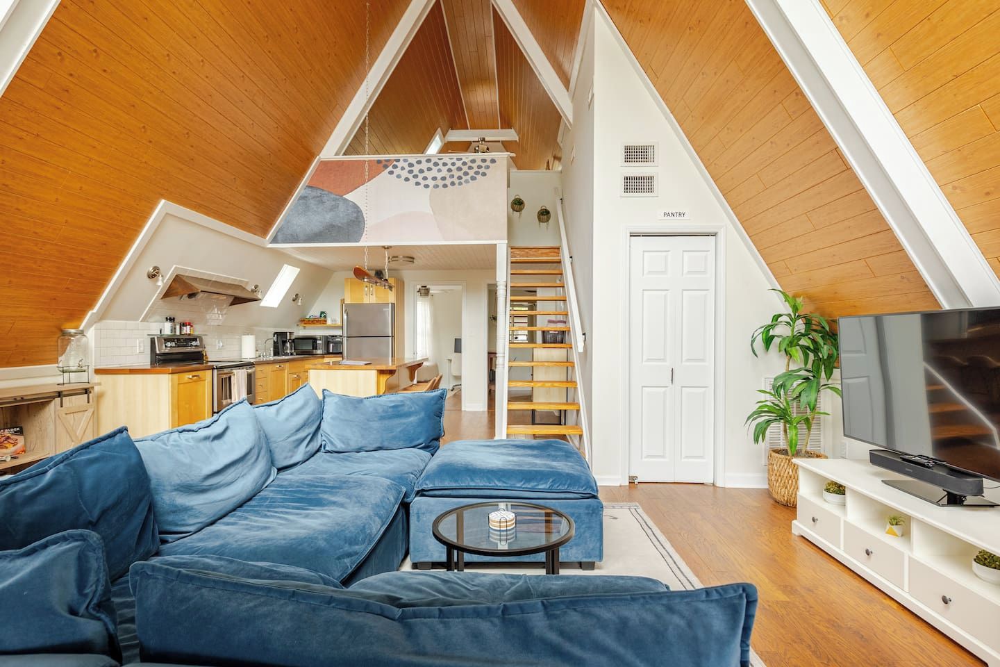 Un espace de vie de style loft avec un plafond en bois, un coin cuisine, un coin repas et une chambre dotée d’un lit en mezzanine.