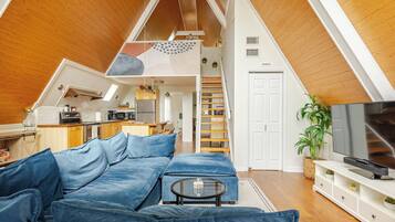 Un espace de vie de style loft avec un plafond en bois, un coin cuisine, un coin repas et une chambre dotée d’un lit en mezzanine.