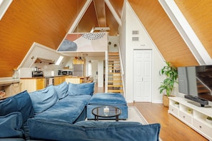 A loft-style living space with a wooden ceiling, a kitchen area, a dining area, and a bedroom with a loft bed.
