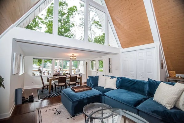 A spacious loft-style living area with a large blue sectional sofa, a glass coffee table, and a dining area with natural light from large windows.