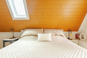 Une chambre avec un plafond en pente, un lit doté d’un matelas matelassé, deux tables de chevet avec des lampes et une lucarne.