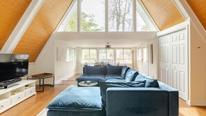 Un dormitorio tipo loft moderno con techo inclinado, ventanas amplias, un sofá modular, un televisor de pantalla plana y piso de madera.