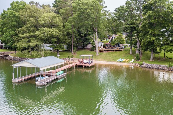 A lakeside property with a dock, a covered seating area, and a house in the background.