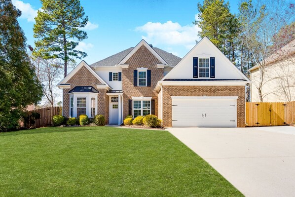 A two-story house with a brick facade, a white garage door, and a well-maintained lawn. - Luxury Atlanta Home(6 Bedrooms) (Atlanta)