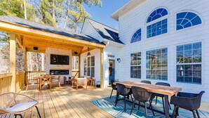 A covered outdoor patio with a wooden deck, a brick fireplace, and a dining area with chairs and a table.
