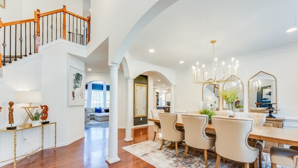 A spacious dining area with a wooden staircase, white columns, and a chandelier.