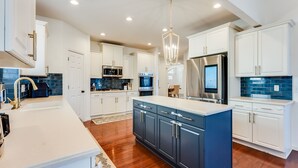 A modern kitchen with white cabinets, a blue island, stainless steel appliances, and a patterned backsplash.