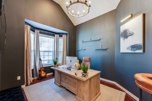 A modern office space with a wooden desk, computer, and decorative items. There is a guitar, a chair, and a large window with curtains. - Luxury Atlanta Home(6 Bedrooms) (Atlanta)